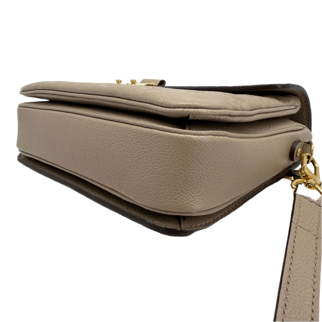 Louis Vuitton Pochette Métis side view showcasing Monogram Empreinte leather in Tourterelle Grey with gold-tone hardware.
