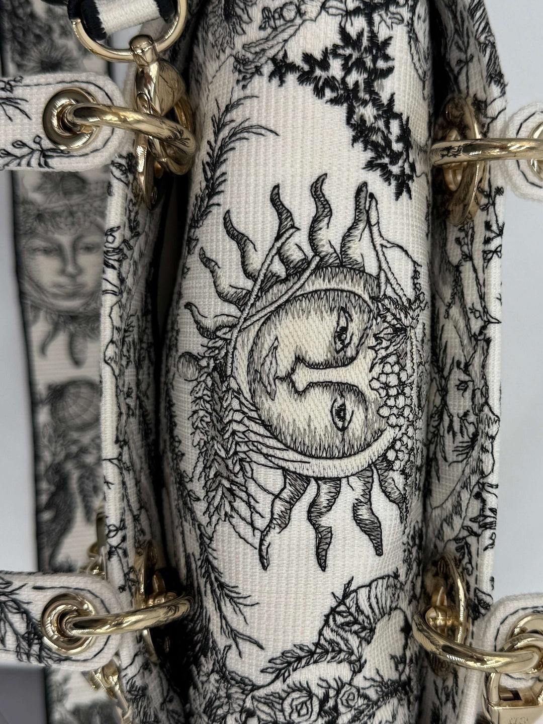 Close-up of embroidered canvas featuring intricate sun and floral designs with gold hardware accents.