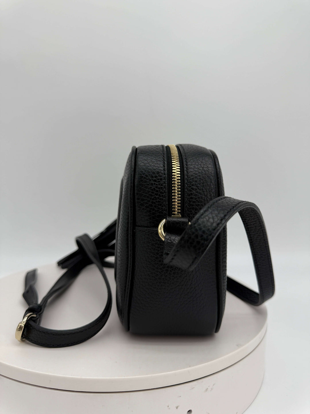 Side view of Gucci Small Soho Disco Bag in black pebbled calfskin leather with gold zipper and strap.