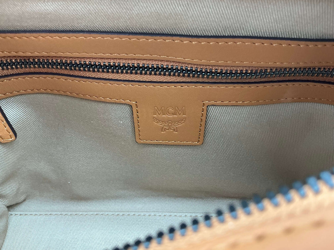 Interior view of an MCM bag showcasing a tan leather zipper pocket and logo tag.