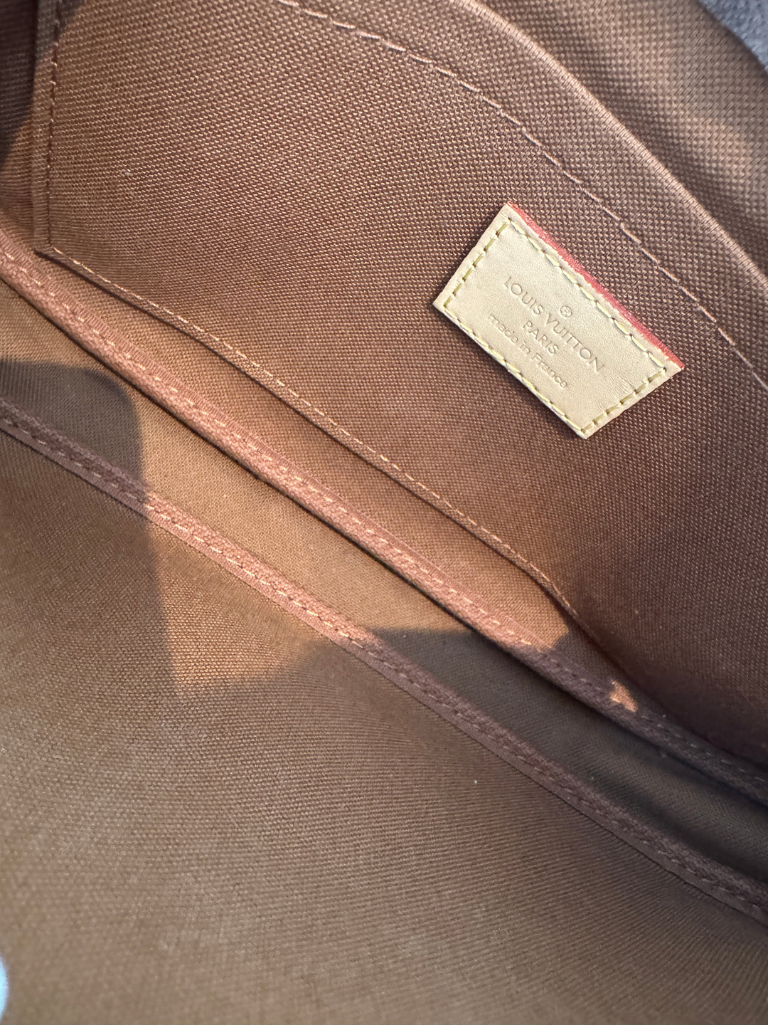 Interior view of LV large pochette showing logo tag and brown lining.