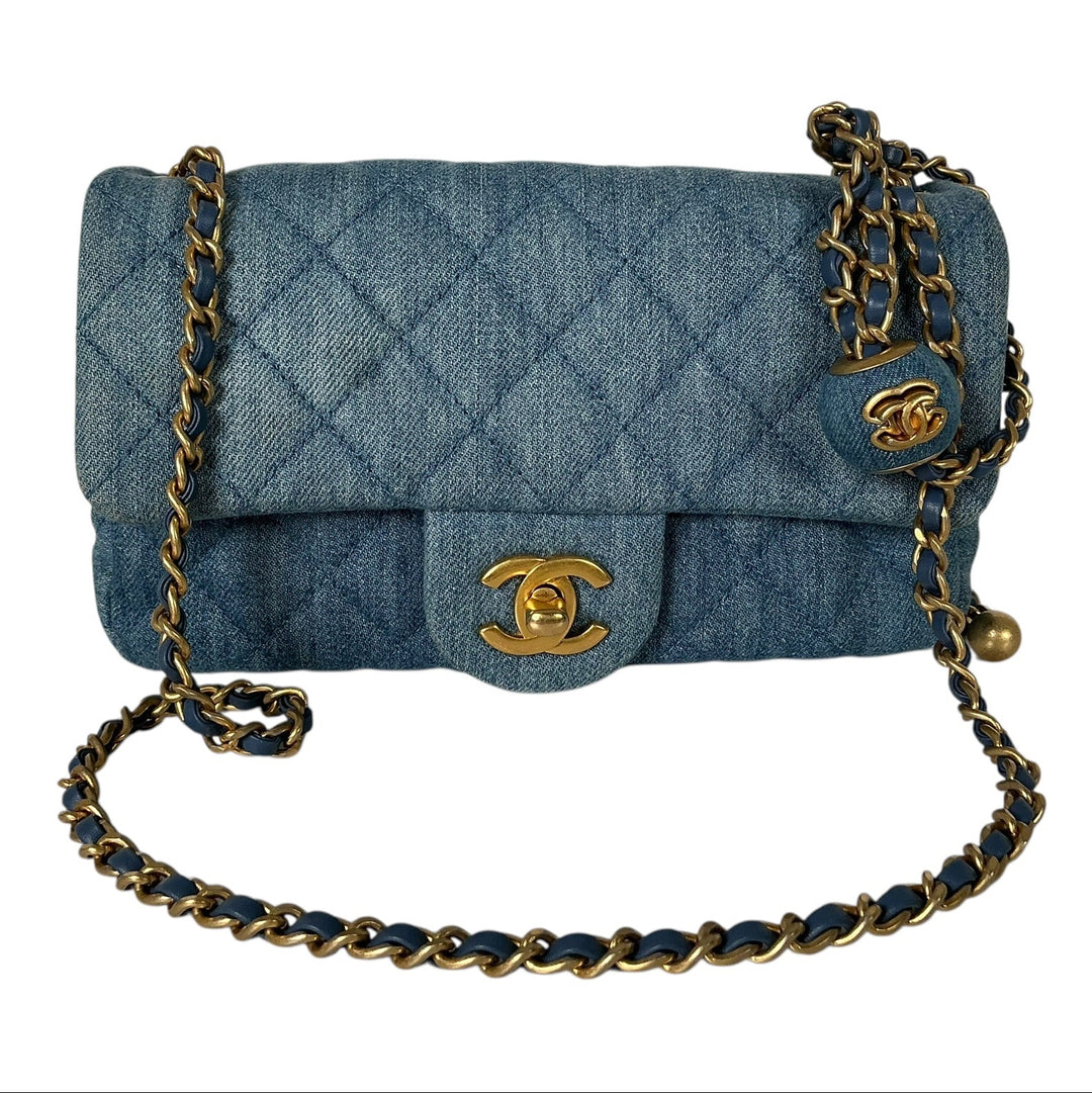 A Chanel quilted flap shoulder bag in blue denim with gold-tone hardware, featuring the interlocking CC logo on the front flap and a chain strap draped across a plain white background.