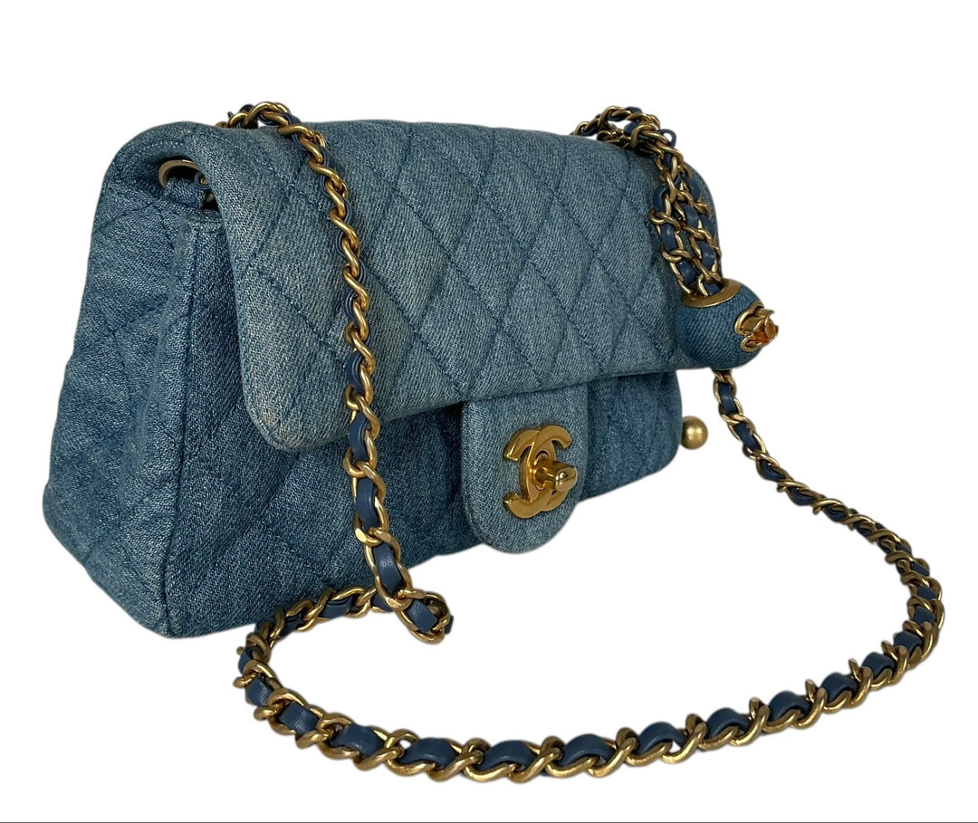 A quilted blue denim shoulder bag with a gold-tone interlocking CC logo and a chain strap with blue leather and gold-tone links, shown on a plain white background.