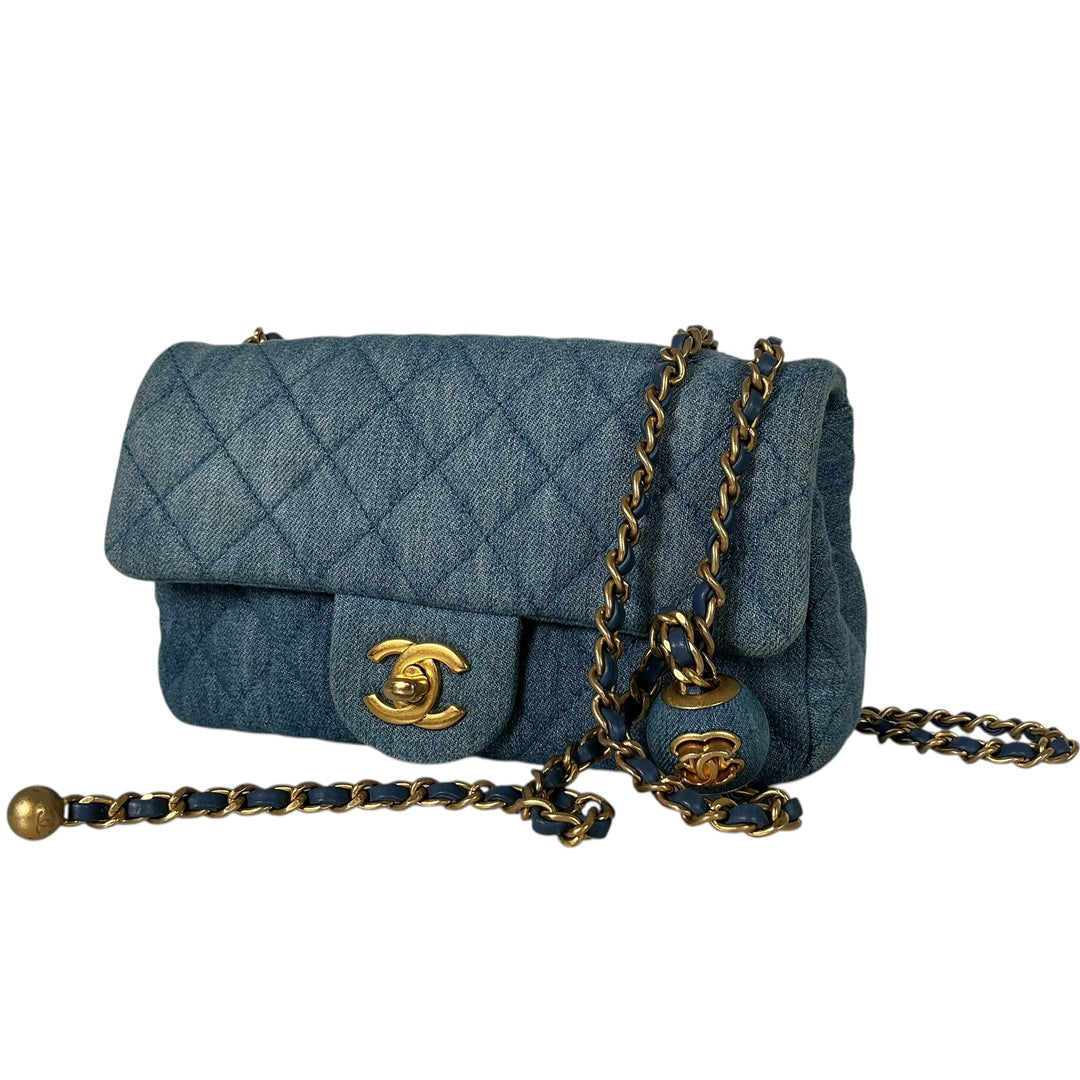 A Chanel Classic Flap handbag in blue denim, featuring the iconic diamond-quilted pattern, gold-tone CC turn-lock, and a blue-and-gold chain strap, shown against a plain white background.