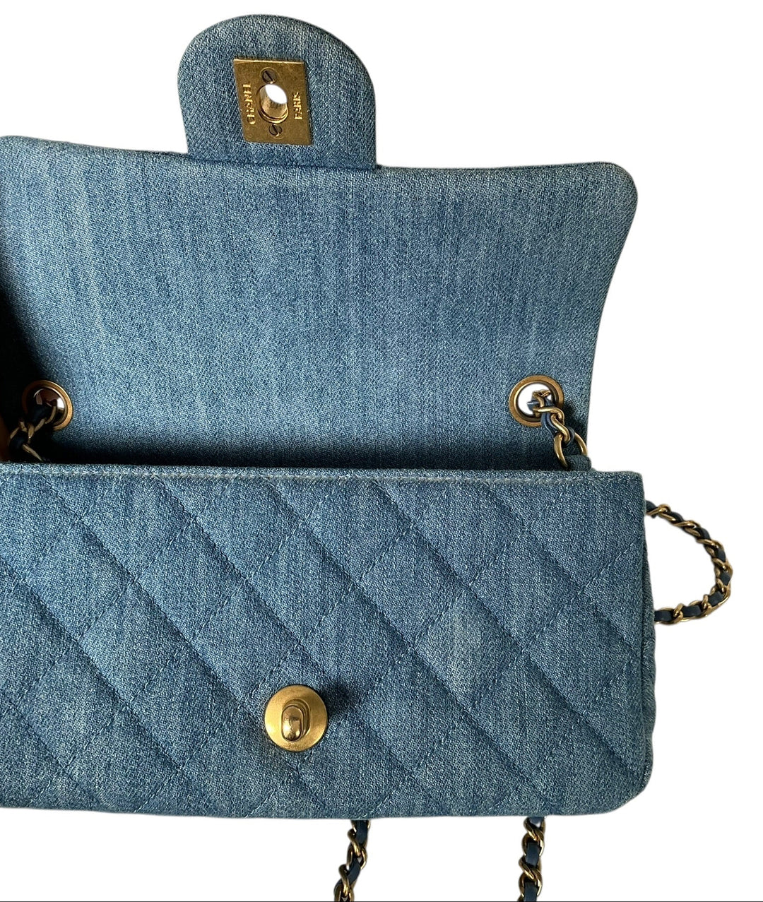 A light blue denim shoulder bag with gold-tone hardware, held open by a hand against a plain white background.