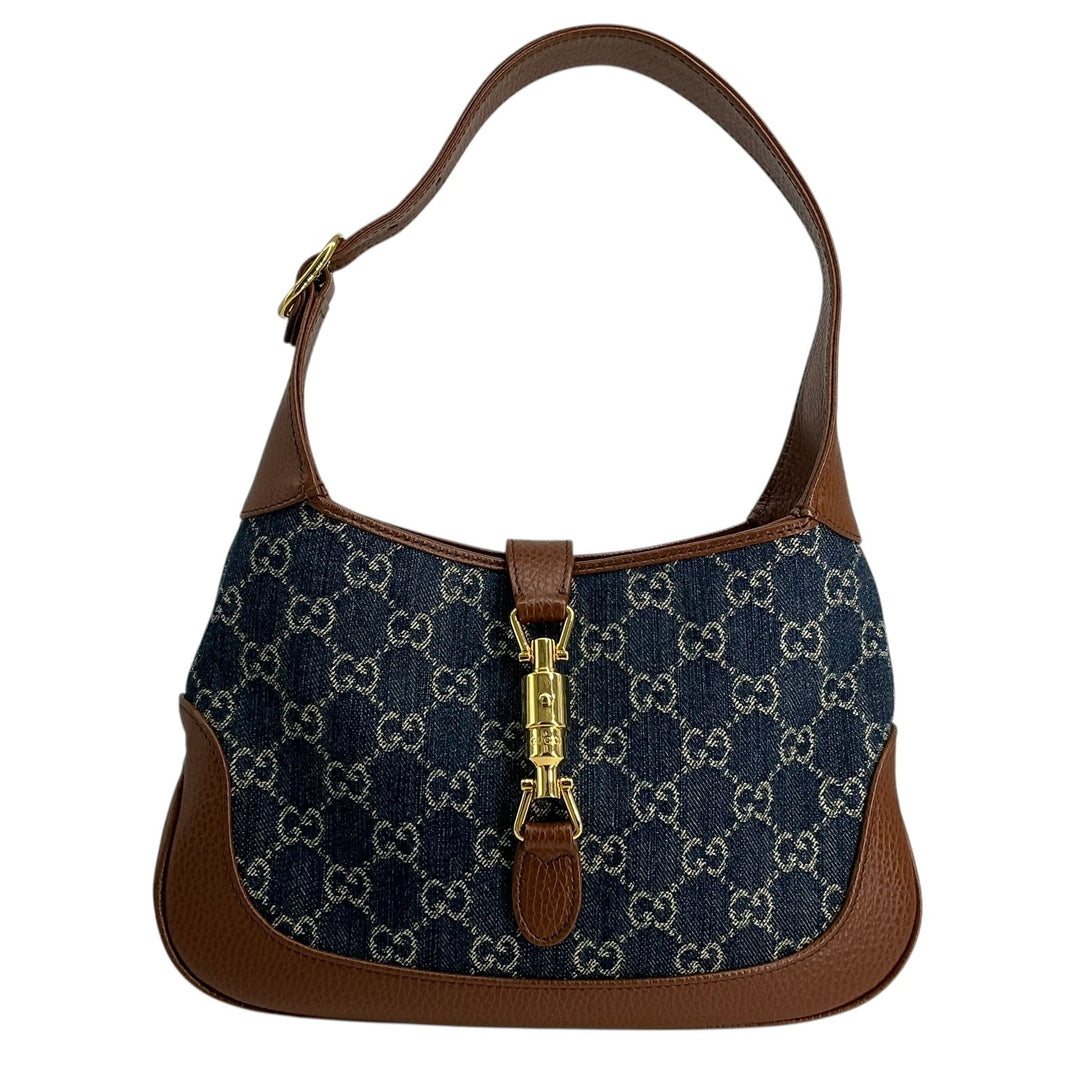 A Gucci shoulder bag featuring navy blue GG Supreme canvas with brown leather trim and a gold-tone turn-lock clasp, shown against a plain white background.