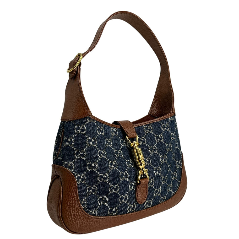 A Gucci shoulder bag featuring the brand's signature GG monogram canvas in navy blue and beige, complemented by brown leather trim and a gold-tone turn-lock closure.