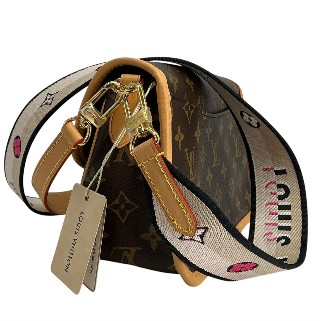 A Louis Vuitton shoulder bag in the classic brown monogram canvas, featuring a wide beige and black branded web strap with pink accents, gold-tone hardware, and a hanging authenticity tag.