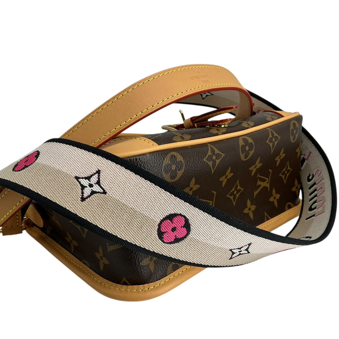 Louis Vuitton monogram canvas shoulder bag with a tan leather handle and a wide cream canvas shoulder strap featuring embroidered pink flowers and black monogram motifs.