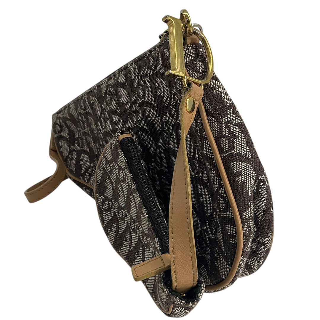 A small shoulder bag with a dark brown and black monogram pattern, tan leather trim, and gold-tone hardware, shown against a plain white background.