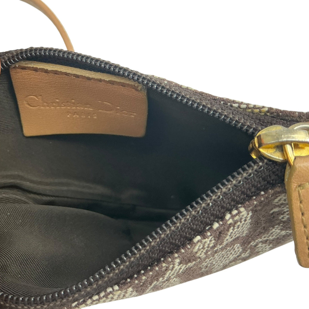 Close-up of an open Christian Dior handbag showing the interior lining, a tan leather brand label, zipper, and part of the patterned exterior with a hand holding it open.