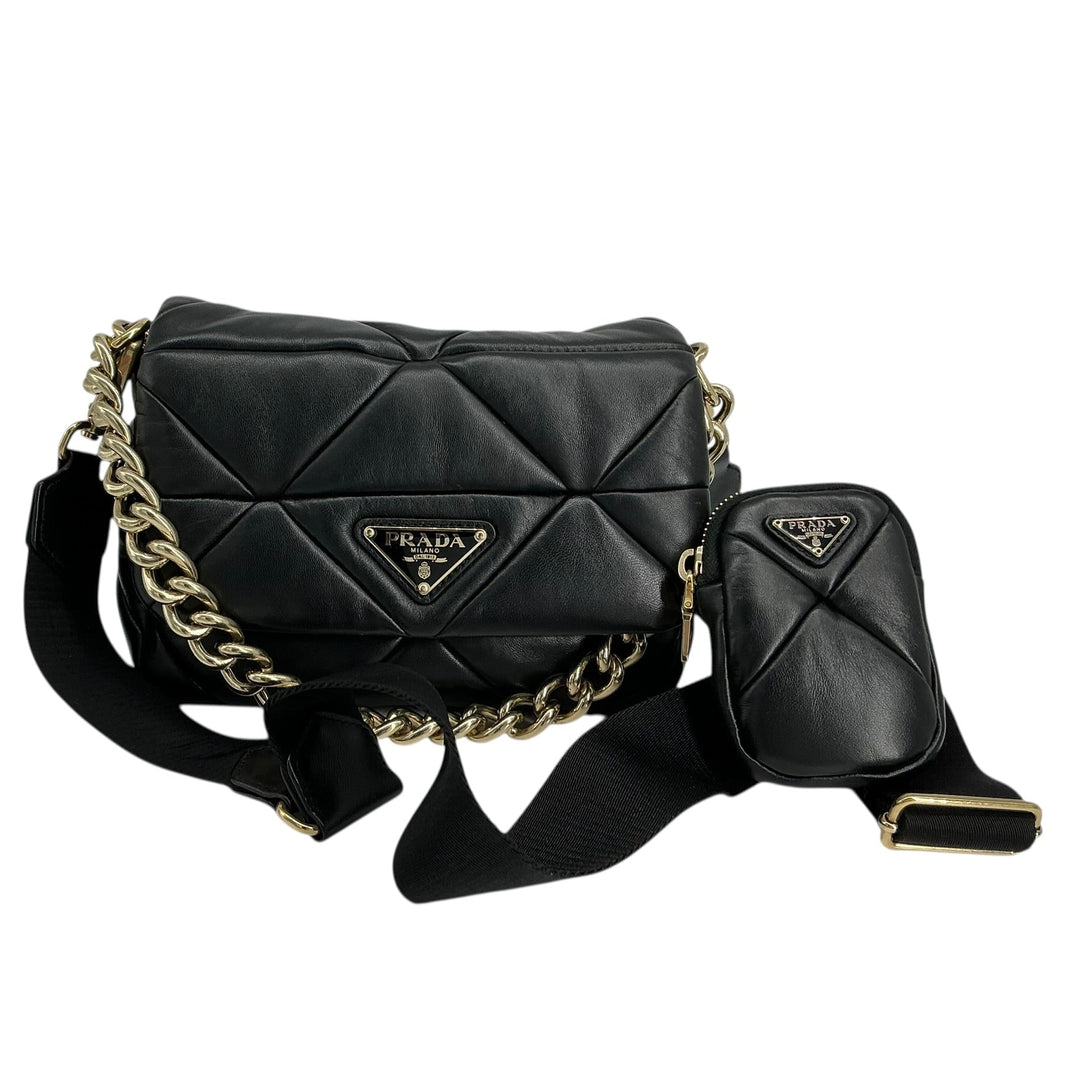 A black quilted leather Prada shoulder bag with a gold chain strap and a matching small pouch, displayed on a clean white background.