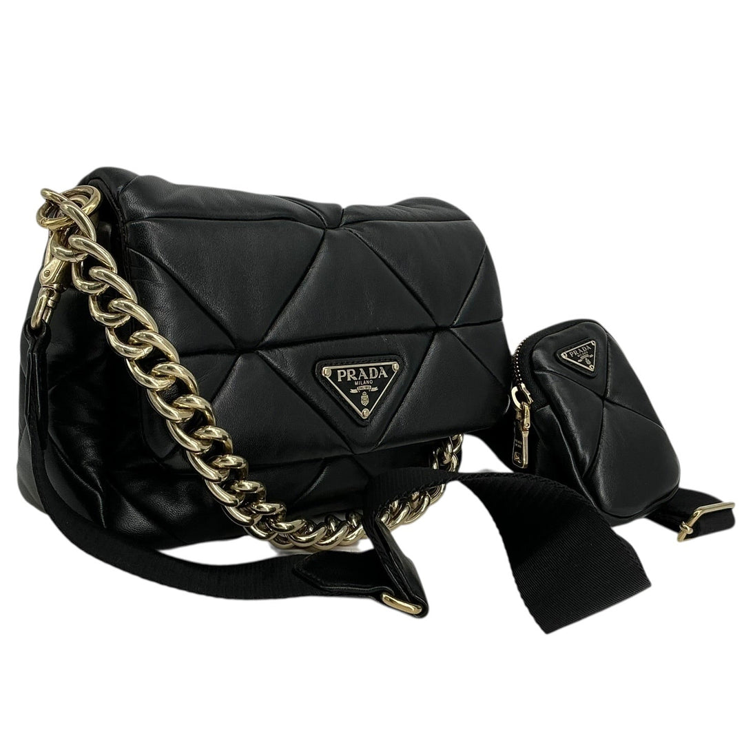 A black Prada quilted leather shoulder bag with a gold chain strap and a small matching pouch, shown on a plain white background.
