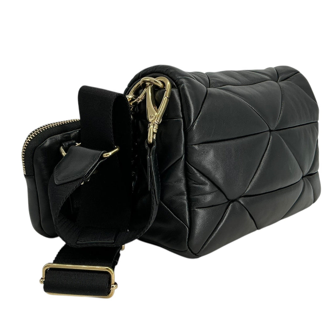 A black quilted leather shoulder bag with gold-tone hardware, shown with its strap detached and laid beside it on a plain white background.