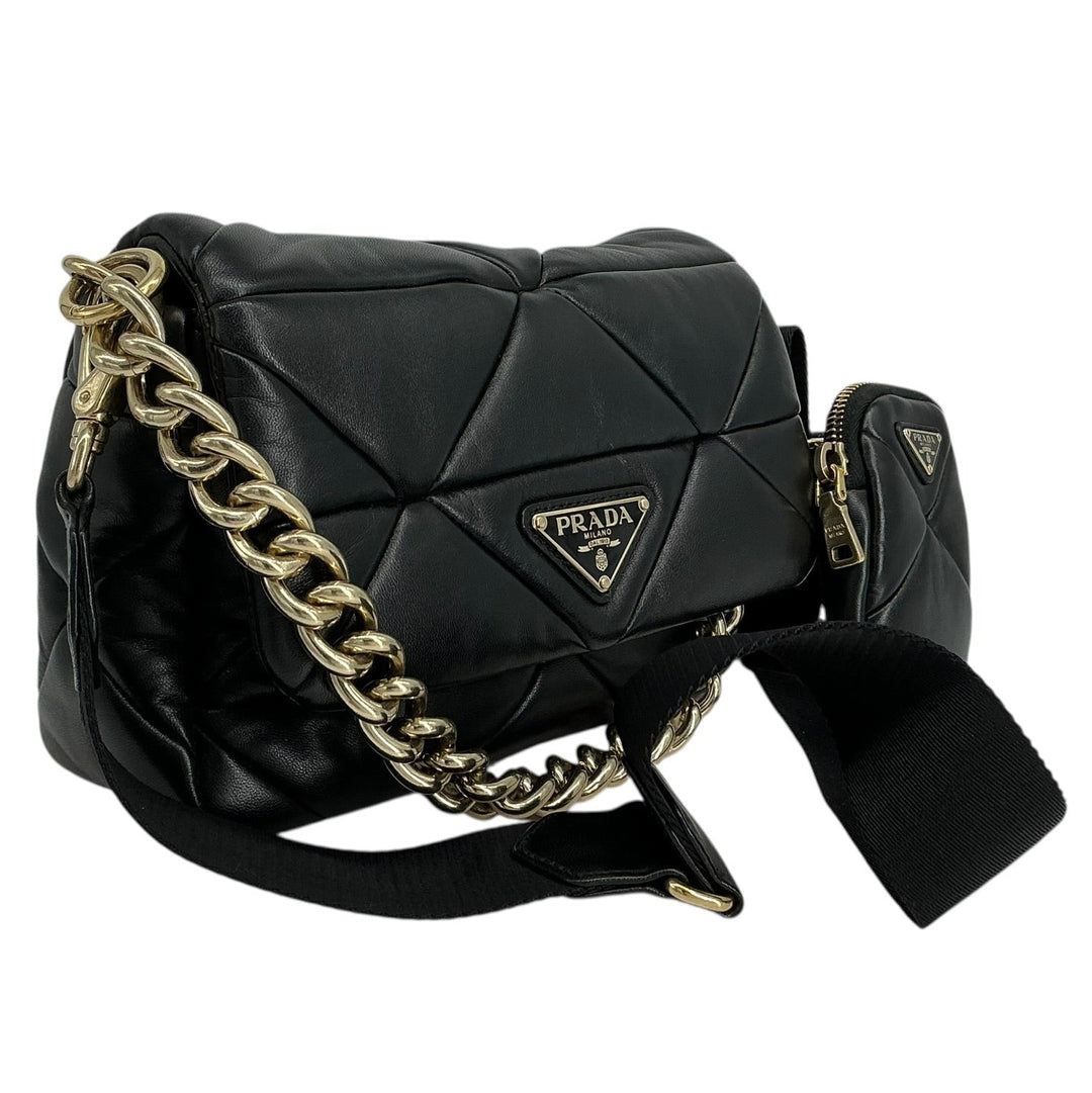 A black Prada quilted leather shoulder bag with a gold-tone chain strap and a small matching pouch, shown on a plain white background.