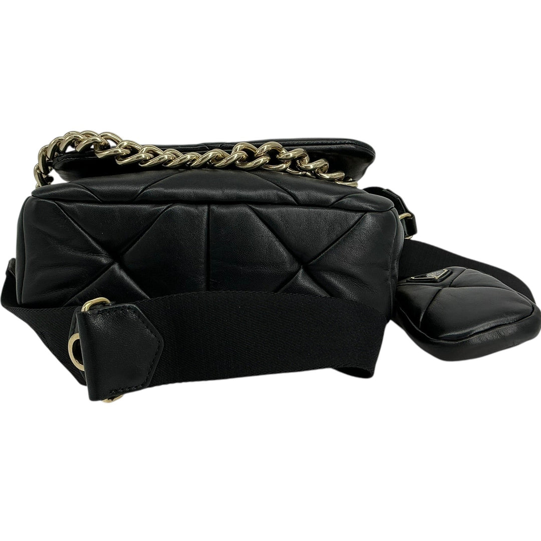 A black quilted leather shoulder bag with a gold-tone chain strap and a matching black fabric shoulder strap, shown against a plain white background.