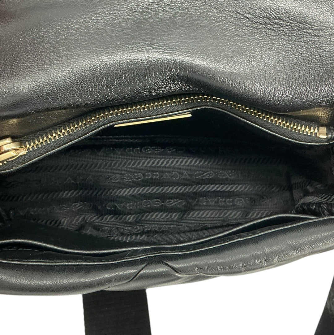 Close-up of a black leather handbag being held open by a hand, showing the interior zip compartment and black patterned lining with gold-tone hardware.