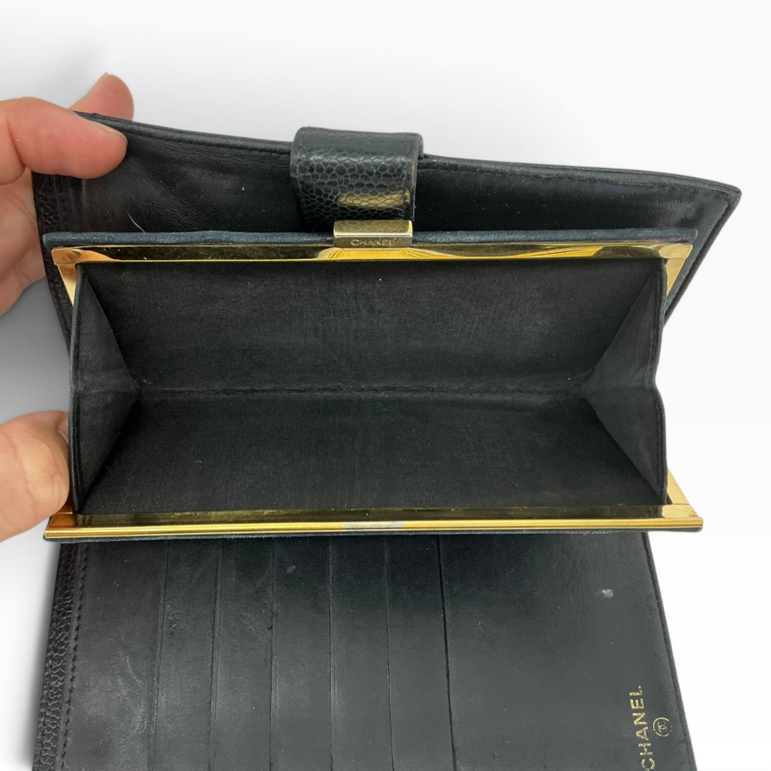 A black leather Chanel wallet with gold-tone hardware, held open by a hand against a plain white background.