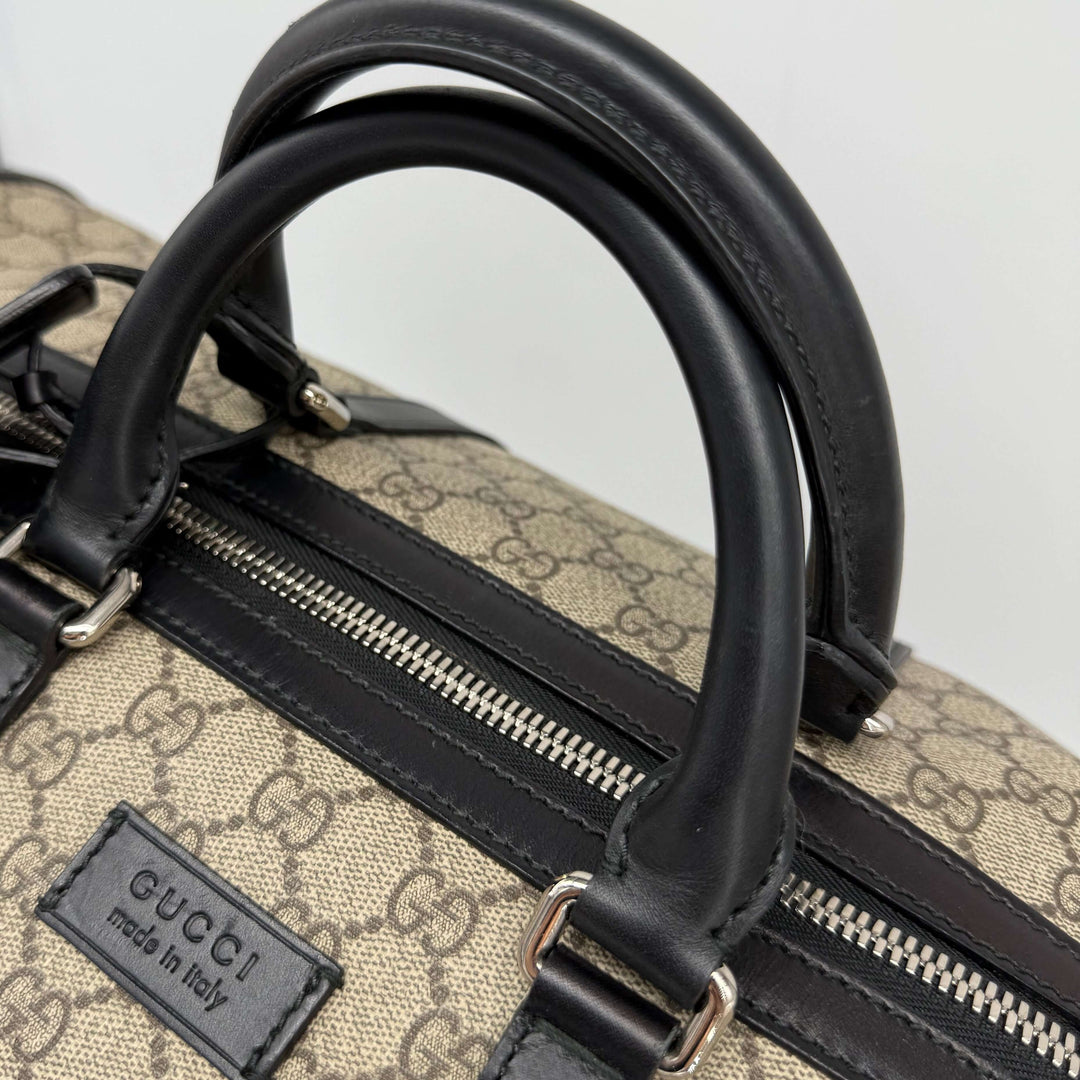 Close-up of the handles on the Authentic Gucci GG Supreme Duffle Carry-on Bag in beige canvas with black leather accents.