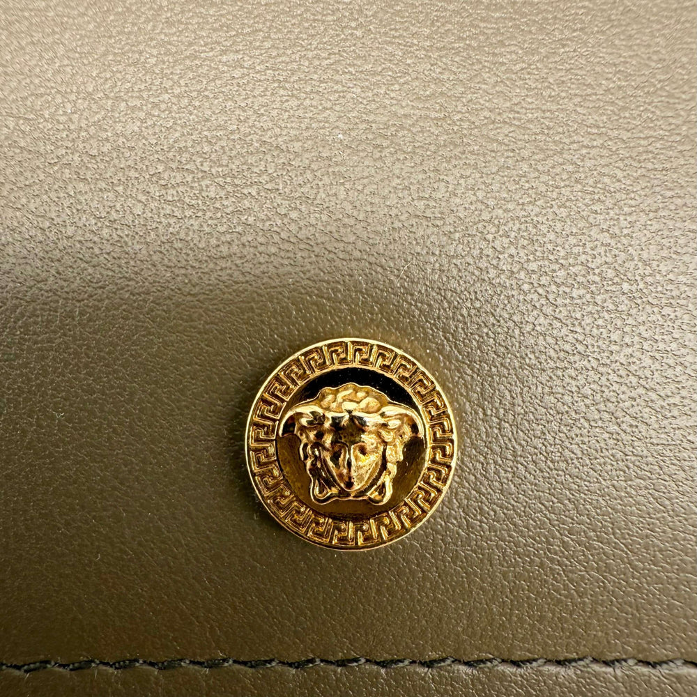 Close-up of the iconic gold Medusa emblem on Versace leather product with intricate Greek key detail.