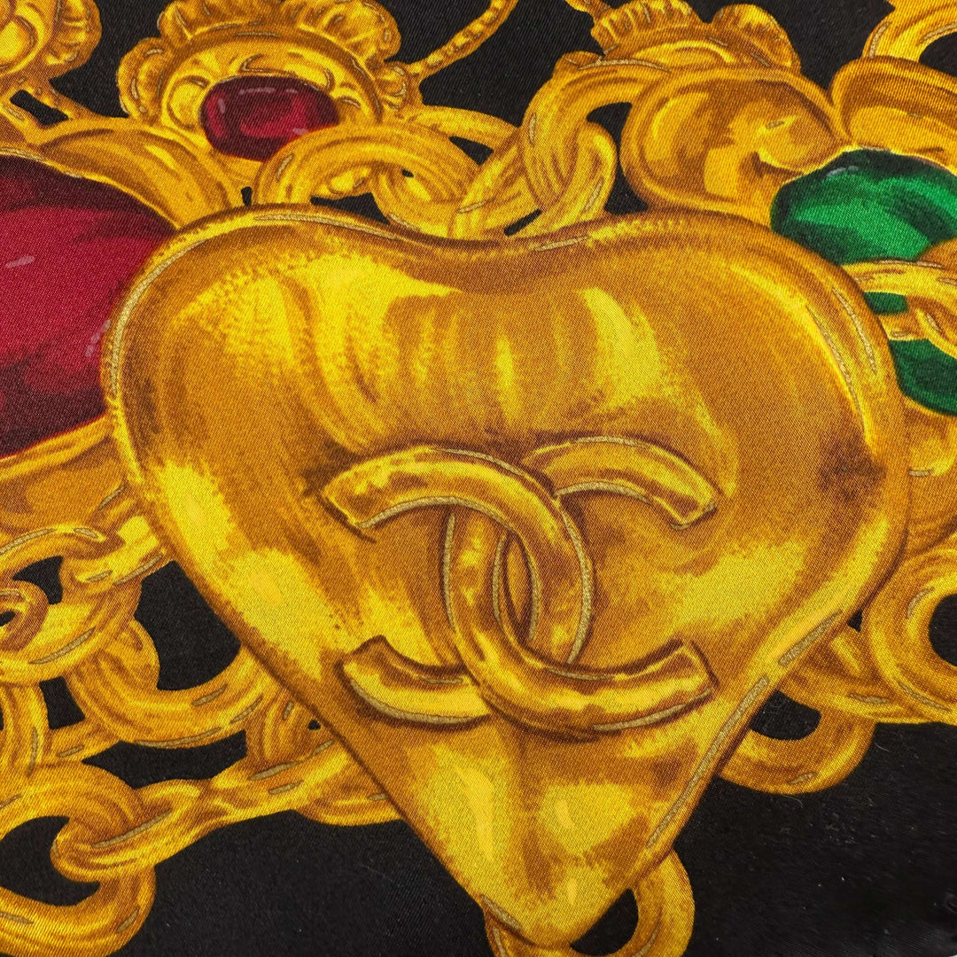 Close-up of CHANEL vintage silk scarf with gold heart motif and jewelry chain design on a black background.