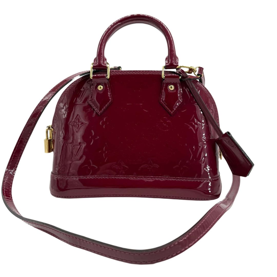 Louis Vuitton Vernis Alma BB in magenta pink patent leather with gold hardware, elegant mini handbag with top handles and adjustable strap.