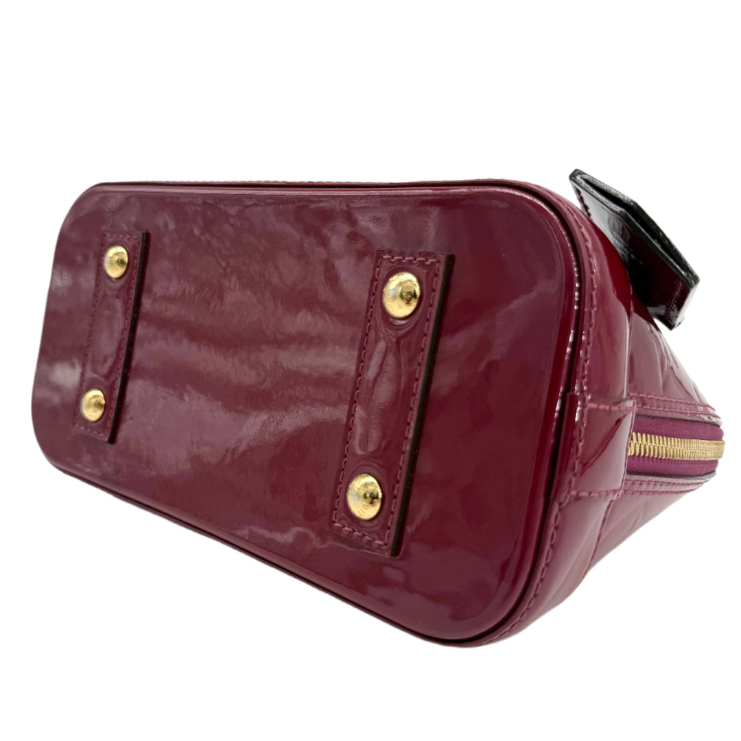 Louis Vuitton Vernis Alma BB base view, magenta patent leather with gold hardware details, showcasing quality craftsmanship.