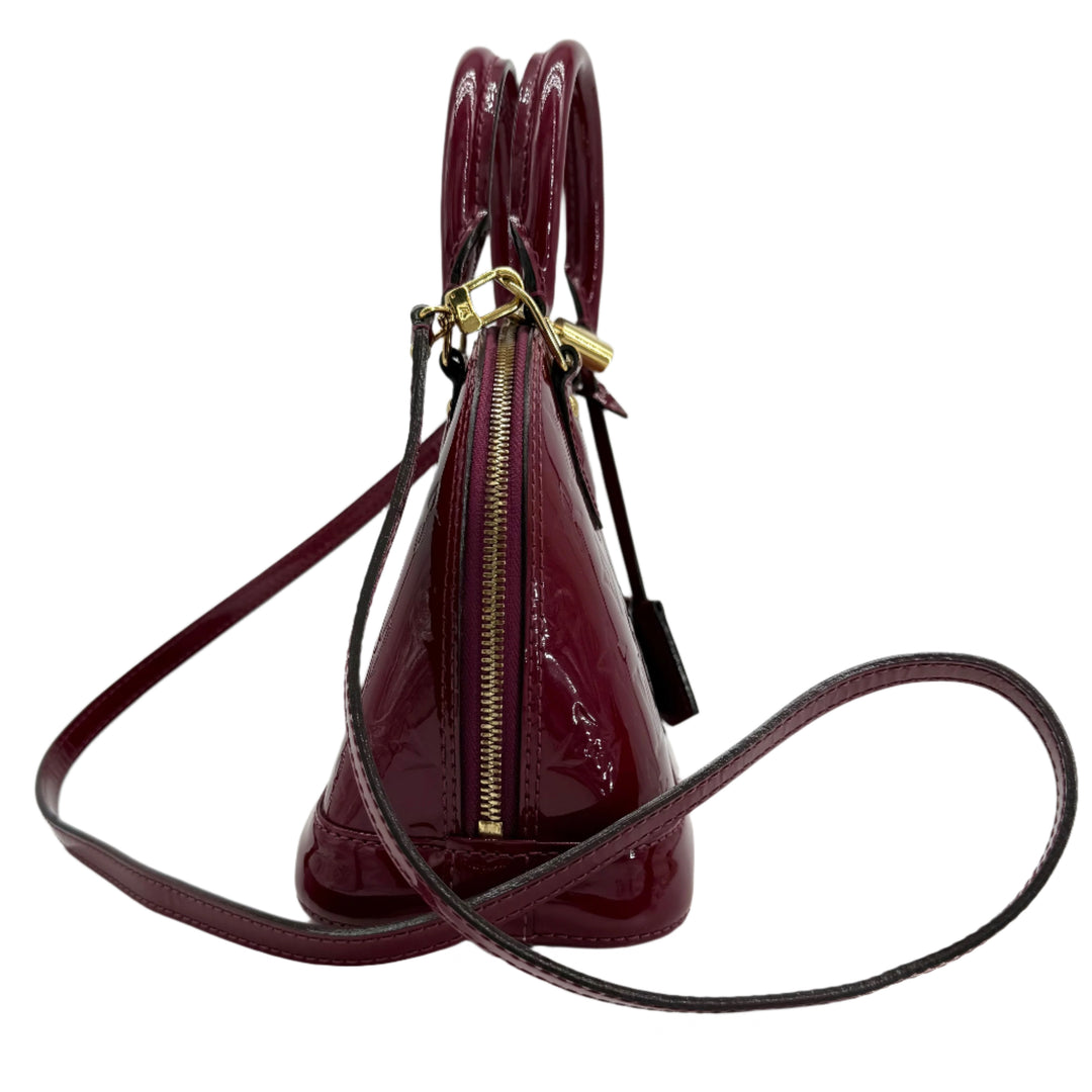 Louis Vuitton Vernis Alma BB bag in magenta patent leather with gold hardware and rolled handles, side view.