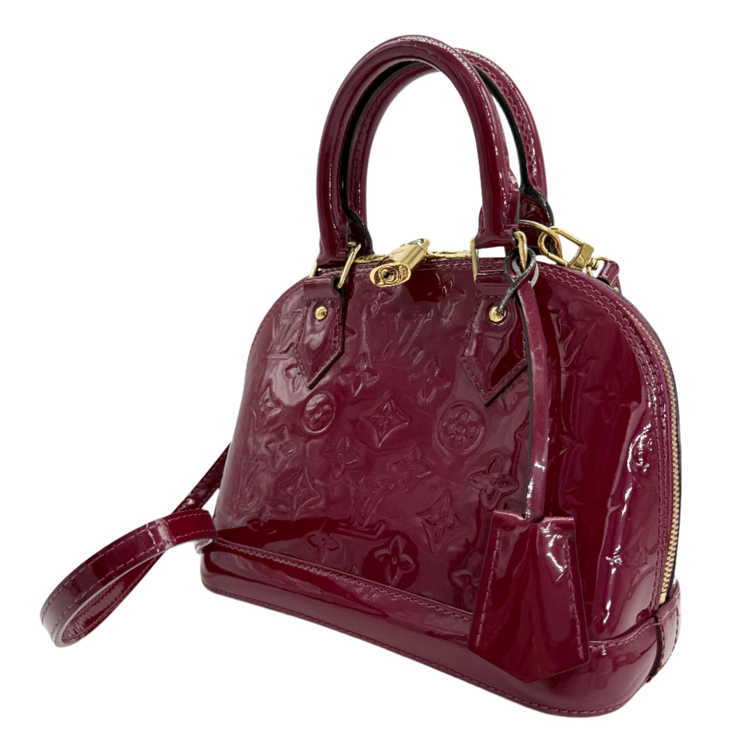 Louis Vuitton Vernis Alma BB in magenta patent leather with gold hardware, featuring structured top handles and a detachable strap.